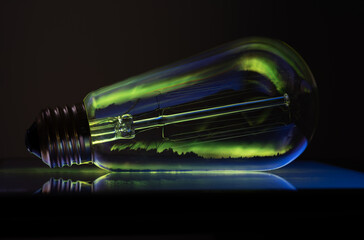Elongate light bulb on a dark background with the Aurora Borealis reflecting through the glass
