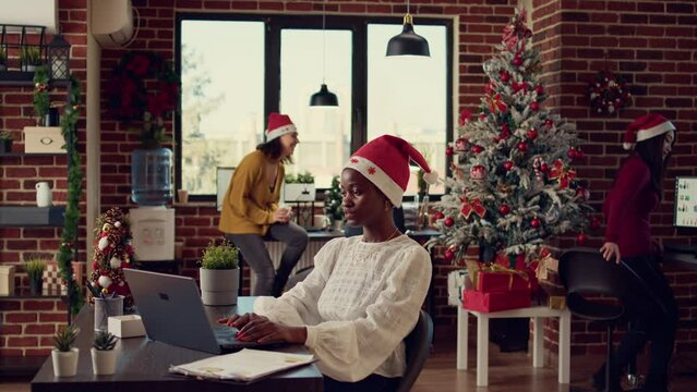 African american coworkers exchanging gifts in festive decorated office, giving presents to celebrate winter holiday season. People feeling joyful during xmas time with seasonal decor.