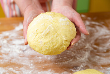 Female hands hold a ball of dough for bread. Flour and portions of dough are on the table. Close-up.