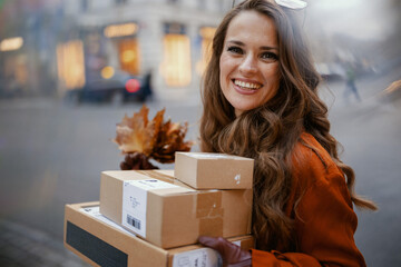 happy trendy woman in orange trench coat with parcels