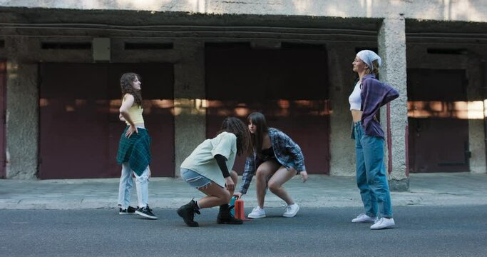 The women put their portable music speakers of color in front of each other. Street dance battle among neighborhood garages of two teenage girl duos.