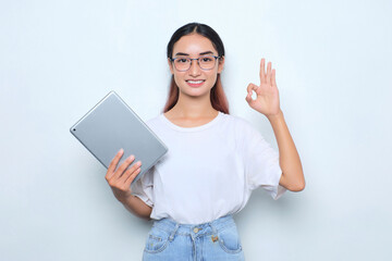Portrait of smiling young Asian girl in white t-shirt holding digital tablet, showing okay sign isolated on white background