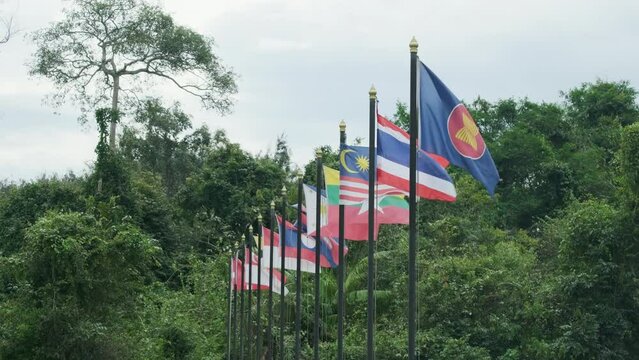 ASEAN community, a group of Southeast Asia country flags waving by the wind on green trees background, Thailand, Malaysia, Myanmar, and other Asian nations with freedom and unity in region relations.
