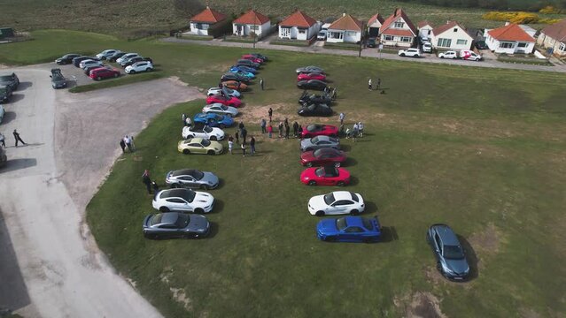 Aerial drone forward moving shot over vertical rows of supercars parked outside the Flamborough Head Lighthouse in Flamborough, UK at daytime.