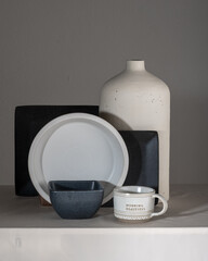 Still life square black matte clay plates and cup and milk jug and vases of various shapes