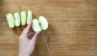 Closeup hand and knife cutting green apple on a wooden chop board. Top View.