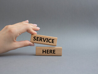 Service here symbol. Concept words Service here on wooden blocks. Beautiful grey background. Businessman hand. Business and Service here concept. Copy space.