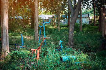 Old outdoor exercise equipment so worn out and covered in trees in outdoor exercise park. Old abandoned gym equipment on sports ground with overgrown grass. Unmaintained abandoned playground.