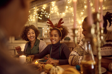 Happy black girl enjoys in Thanksgiving meal with her family at dining table.