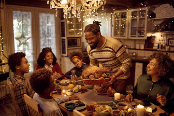 Happy African American man serving stuffed turkey while having dinner with his extended family in...
