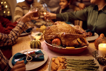 Close up of stuffed turkey during Thanksgiving meal with family toasting in background.
