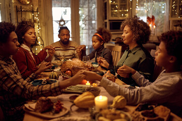 African American extended family saying grace while having Thanksgiving meal at dining table. - Powered by Adobe