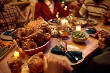 Close up of roast turkey with family saying grace at dining table on Thanksgiving.