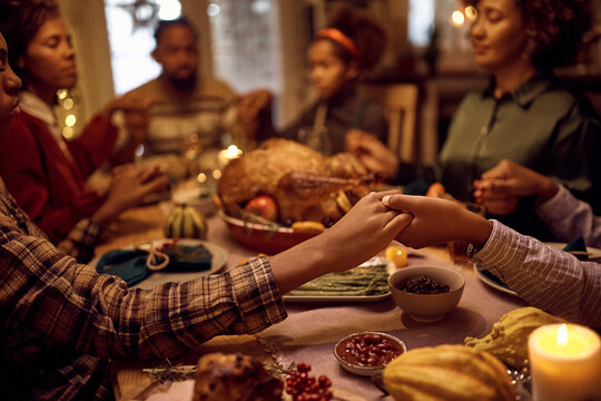 Close up of black brothers holding hands while praying with their family during dinner on Thanksgiving.