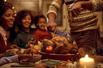 Close up of black father carving Thanksgiving turkey during family lunch at dining table