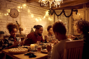 Happy black man eating dinner with his family while celebrating Thanksgiving at dining table.