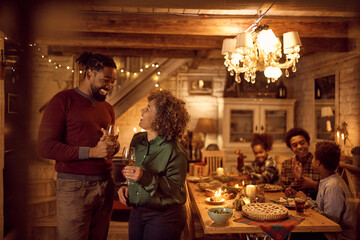 Happy black man and his mother laugh while drinking wine in dining room on Thanksgiving.