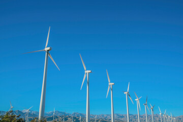 Row of windmills with three blades against blue sky on a sunny day.