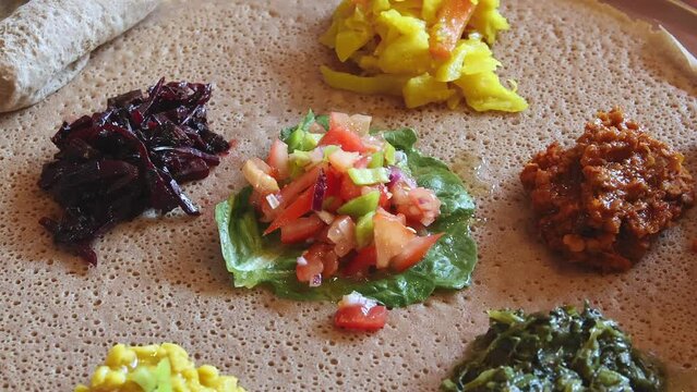 Enjoying an Ethiopian meal of injera, with shiro, lentils and a variety of vegetables.  Slow motion.
