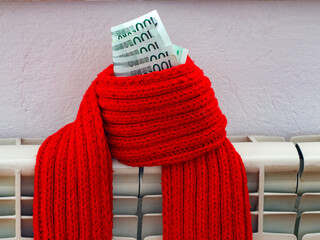 100 euro banknotes and red scarf on a central heating radiator, the concept of expensive heating costs, close-up