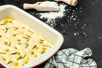 Raw focaccia dough with rosemary on a dark background. banner, menu, recipe place for text, top view