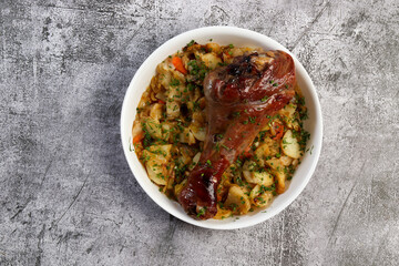 Oven baked Turkey drumstick with potatoes and vegetables in a white baking dish on a dark grey background. Top view, flat lay
