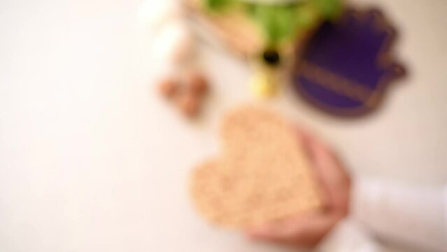 selective focus, blurred woman's hands holds Matzah shape of heart. Traditional of Jewish Holiday on Passover. Home symbol of lovely family. top view, layout. love and care. Space for text.