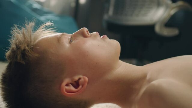Thoughtful boy lays on the carpetted floor thinks about his soccer match with school sports team. Determined young boy with bare upper body in his room.