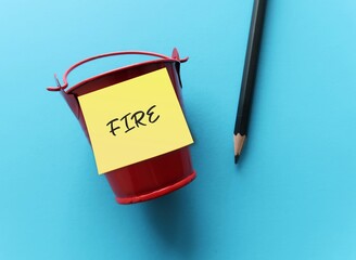 Pencil on blue background with stick note on red tub FIRE (financial independence + retire early)...