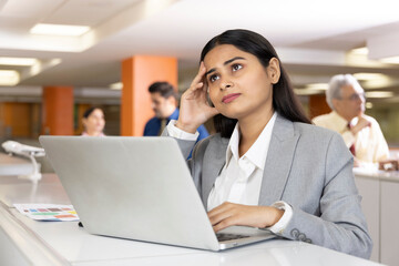 Thoughtful millennial professional solving problems using laptop in office.