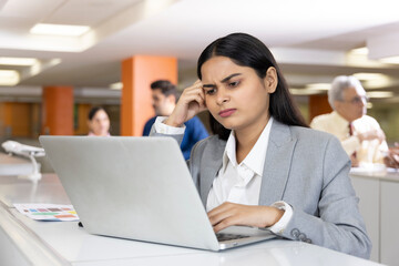 Thoughtful millennial professional solving problems using laptop in office.