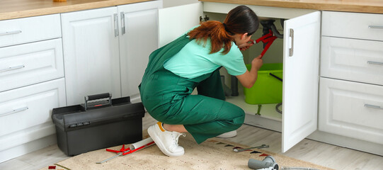 Female plumber fixing sink in kitchen - obrazy, fototapety, plakaty