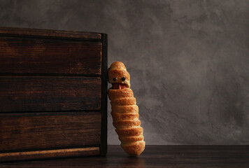 sausage in the dough in the form of a mummy on a gray background with a wooden box for the...