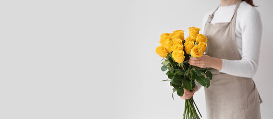 Female florist holding beautiful yellow roses on light background with space for text