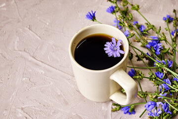 chicory drink and floating chicory flower in a coffee mug next to chicory flowers