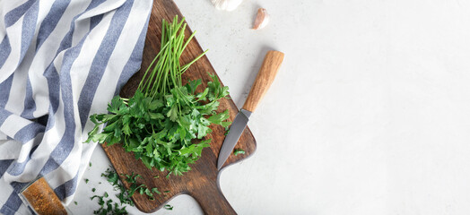 Cutting board, fresh parsley and knife on light background with space for text