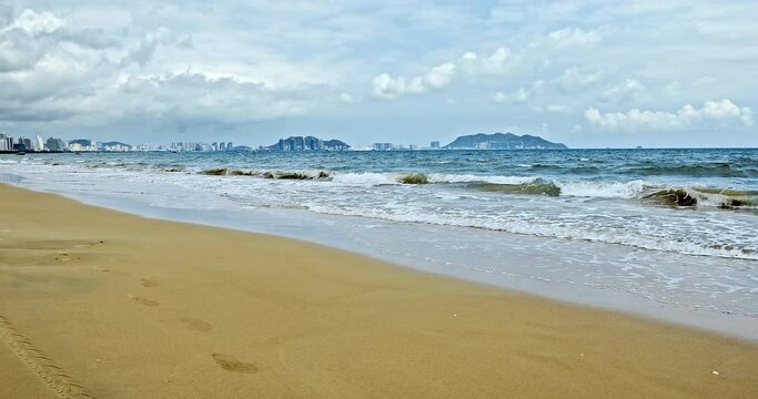 Rolling waves and city skyline in Sanya, Hainan Island, China. Beautiful seascape. Yellow sand beach, azure sea and blue sky.