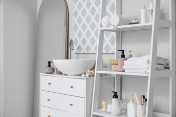 Fototapeta na wymiar Shelf unit with different bath accessories and modern sink near light wall