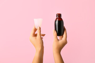 Woman with bottle of cough syrup and cup on pink background