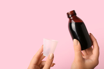 Woman with bottle of cough syrup and cup on pink background