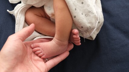産後1か月の0歳児の新生児の足に大人が手を添えている写真