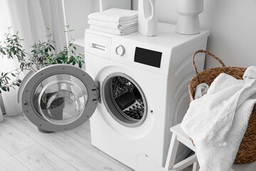 Modern washing machine with towels and detergent in laundry room