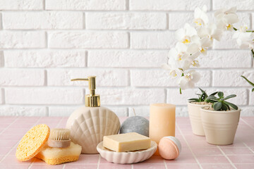 Obraz na płótnie Canvas Set of bath supplies with houseplants on table near light brick wall