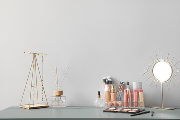 Organizer with decorative cosmetics, mirror, reed diffuser and jewelry on table near light wall