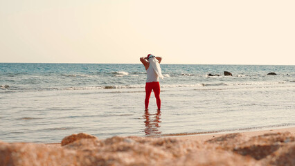 Santa Claus sunbathes. Santa Claus having fun. Funny Santa, in sunglasses, standing in sea water on the beach. Santa Claus summer vacation. High quality photo