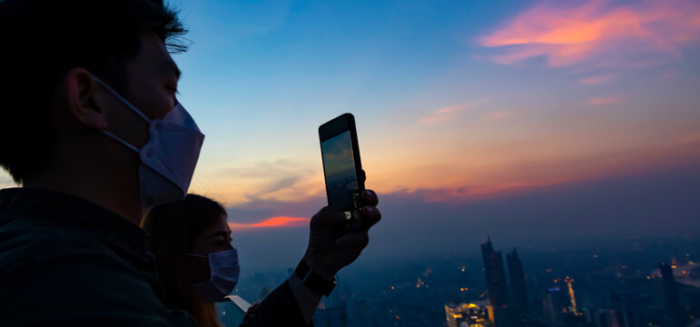 Happy lifestyle with young couple take a picture by Photo camera of a smartphone with sunset sky  scene in the cityscape on the rooftop view