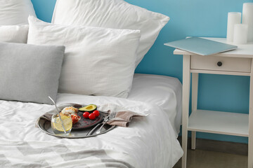 Tray with delicious breakfast and glass of water on bed