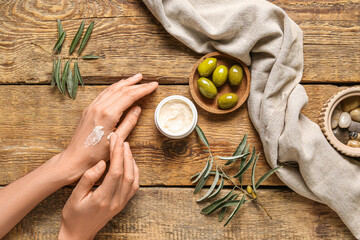Woman applying natural olive cream onto her hand on wooden background