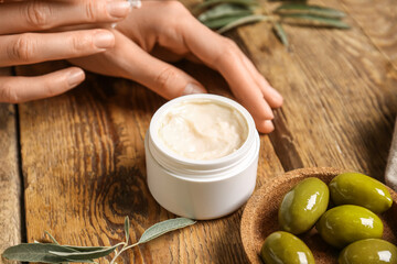 Female hands with jar of natural olive cream on wooden table, closeup