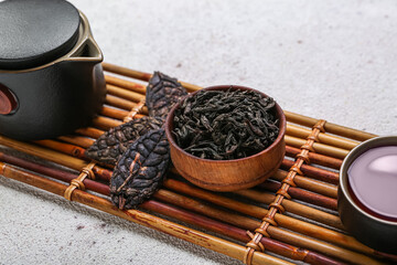 Bamboo mat with bowl of dry puer tea, cup and teapot on white background